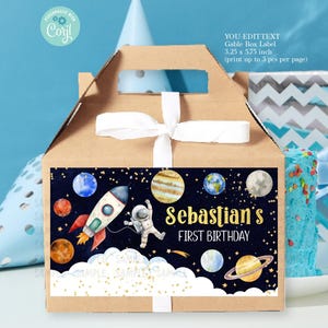 May include: A brown gable box with a white ribbon and a label featuring a watercolor illustration of a rocket, astronaut, and planets. The label says "Sebastian's First Birthday".