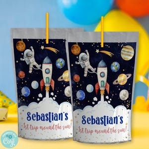 May include: Two blue and white juice pouches with a space theme. The pouches feature a cartoon astronaut riding a rocket through space. The text on the pouches reads "Sebastian's 1st trip around the sun!"
