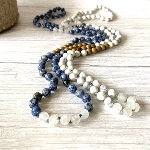 May include: A multi-strand mala necklace with blue, white, and brown beads. The necklace is made of natural stones and is a beautiful and unique piece of jewelry.