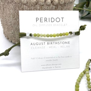 Può includere: Braccialetto diffusore di olio in pietra di peridoto verde con perline d'argento e cordoncino in pelle scamosciata verde. La carta riporta "Peridot Oil Diffuser Bracelet", "August Birthstone", "Cleanse - Heal - Relax", "Add 1-2 drops of essential oil to the faux suede or wooden beads", "www.albion-design.com", "Handmade in Surrey".