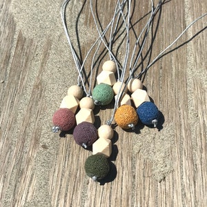 May include: A set of seven necklaces featuring lava stone and wooden beads. The necklaces come in a variety of colours, including green, blue, brown, and yellow. The necklaces are strung on grey cords.