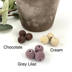 May include: Three sets of colorful ceramic beads in chocolate, cream, and grey lilac colors. The beads are round and have a textured surface.