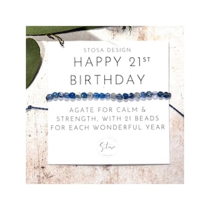 Op de afbeelding: Een kaart met de tekst "STOSA DESIGN HAPPY 21ST BIRTHDAY AGATE FOR CALM & STRENGTH, WITH 21 BEADS FOR EACH WONDERFUL YEAR" en een blauwe agaten armband.