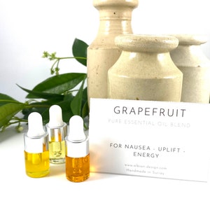May include: Three small amber glass bottles with silver droppers filled with essential oil. The bottles are on a white surface with a white card that reads "GRAPEFRUIT PURE ESSENTIAL OIL BLEND FOR NAUSEA - UPLIFT. ENERGY www.albion-design.com Handmade in Surrey"