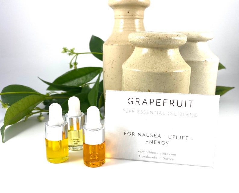 May include: Three small amber glass bottles with silver droppers filled with essential oil. The bottles are on a white surface with a white card that reads "GRAPEFRUIT PURE ESSENTIAL OIL BLEND FOR NAUSEA - UPLIFT. ENERGY www.albion-design.com Handmade in Surrey"