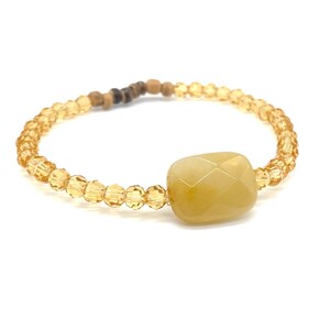 May include: A yellow crystal bead bracelet with a large, faceted, yellow gemstone charm.