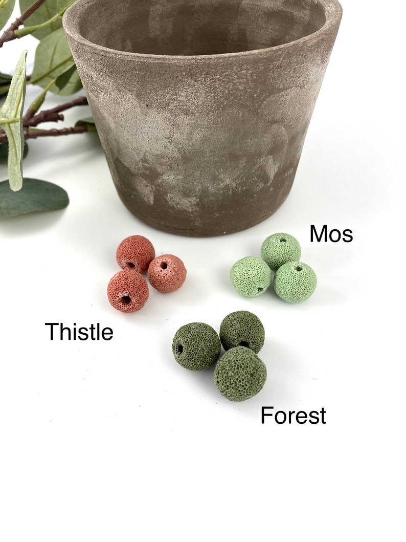 May include: Four red lava rock beads labeled "Thistle" and four green lava rock beads labeled "Mos" and "Forest" on a white surface.