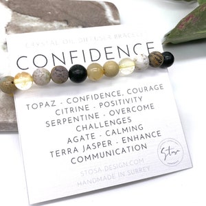 May include: A bracelet made with various semi-precious stones, including topaz, citrine, serpentine, agate, and terra jasper. The bracelet is on a white card with the word "CONFIDENCE" in black lettering and a description of the stones and their meanings.