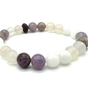 May include: A bracelet made of white, grey, and purple beads. The bracelet features a variety of different beads, including some that are round and some that are oval.