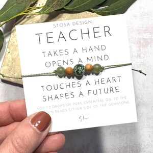 Puede incluir: Un brazalete de cuentas verdes y marrones con una tarjeta que dice "Teacher Takes a Hand Opens a Mind Touches a Heart Shapes a Future". Agrega 1-2 gotas de aceite esencial puro a las cuentas de madera a cada lado de la piedra preciosa.