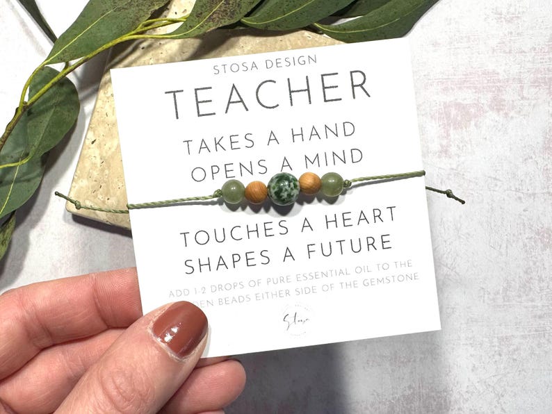 Puede incluir: Un brazalete de cuentas verdes y marrones con una tarjeta que dice "Teacher Takes a Hand Opens a Mind Touches a Heart Shapes a Future". Agrega 1-2 gotas de aceite esencial puro a las cuentas de madera a cada lado de la piedra preciosa.