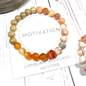 Può includere: Due braccialetti di perline con le parole "Crystal Jewellery" e "Motivation" su un cartoncino bianco. I braccialetti sono realizzati con perline di cornalina, avventurina e legno. Il cartoncino riporta anche la scritta "Cornalina - Aventurina - Pietra di rete".