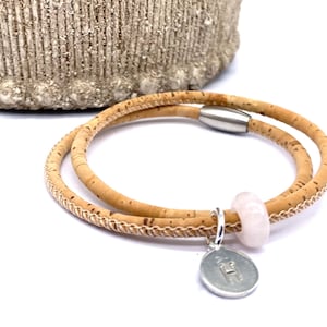 May include: A double-wrap cork bracelet with a silver charm and a pink stone bead. The bracelet has a magnetic clasp.