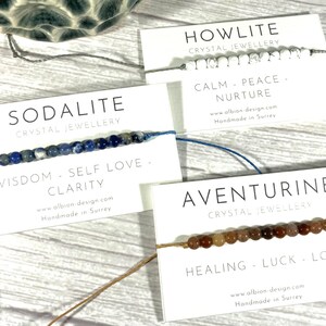 Op de afbeelding: Drie armbanden gemaakt met verschillende soorten kristallen. De armbanden liggen op witte kaartjes met de naam van het kristal, de eigenschappen van het kristal en de website en locatie van de maker. De kristallen zijn howliet, sodaliet en aventurijn.