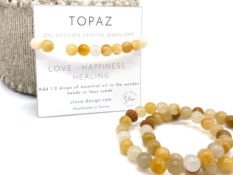 Pu&ograve; includere: Due braccialetti di cristallo di topazio con perline di legno. I braccialetti sono fatti di perline di colore giallo chiaro, bianco e marrone. La carta recita "TOPAZ OIL DIFFUSER CRYSTAL JEWELLERY LOVE - HAPPINESS - HEALING Add 1-2 drops of essential oil to the wooden beads or faux suede stosa-design.com Handmade in Surrey"