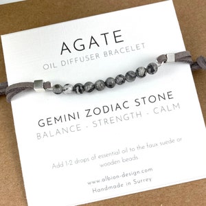 May include: Gray agate stone diffuser bracelet with a grey suede cord. The bracelet is labelled "Gemini Zodiac Stone Balance - Strength - Calm".