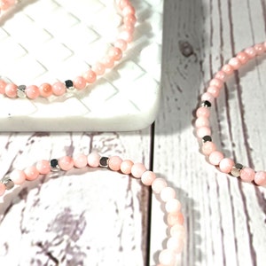 Op de afbeelding: Drie roze kralenarmbanden met zilveren accenten. De armbanden liggen op elkaar gestapeld op een wit oppervlak.