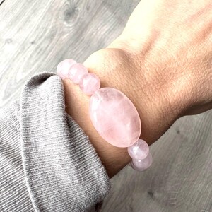 Könnte beinhalten: Ein Armband aus rosa Rosenquarz mit ovalen Perlen. Das Armband befindet sich an einem Handgelenk.
