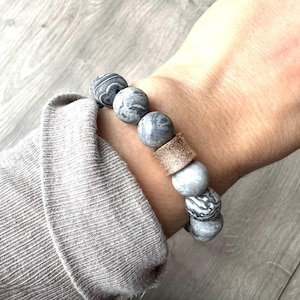 Op de afbeelding: Grijs en wit marmerachtig stenen kralen armband met een gouden accentkraal.