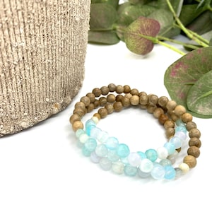 May include: A set of three bracelets, one with light blue and white beads, and two with brown wooden beads.