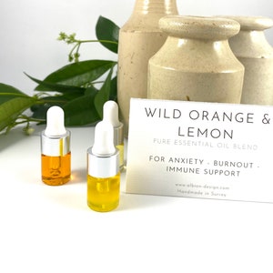 May include: Three small glass bottles with silver caps and droppers filled with a yellow liquid. The bottles are on a white surface with a white card that reads "WILD ORANGE & LEMON PURE ESSENTIAL OIL BLEND FOR ANXIETY BURNOUT IMMUNE SUPPORT www.albion-design.com Handmade in Surrey"