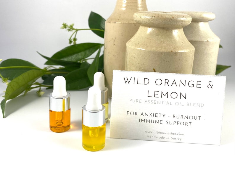 May include: Three small glass bottles with silver caps and droppers filled with a yellow liquid. The bottles are on a white surface with a white card that reads "WILD ORANGE & LEMON PURE ESSENTIAL OIL BLEND FOR ANXIETY BURNOUT IMMUNE SUPPORT www.albion-design.com Handmade in Surrey"