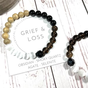 Puede incluir: Dos pulseras de cristal con el texto "GRIEF & LOSS" y las palabras "OBSIDIAN - SMOKY QUARTZ - AGATE - SELENITE" en una tarjeta blanca. Las pulseras están hechas con cuentas marrones, negras y blancas.