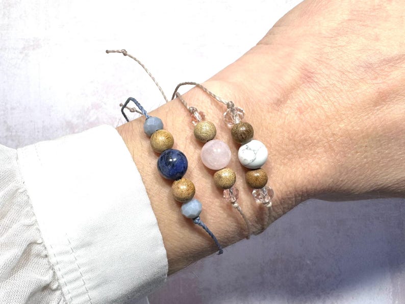 May include: Three bracelets with wooden beads and gemstone accents. The bracelets are made with natural materials and feature a blue, pink, and white gemstone.