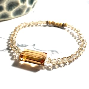 May include: A delicate bracelet made with clear glass beads and a single amber-coloured crystal bead.