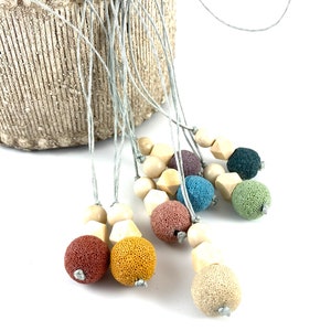 May include: A set of colorful lava stone and wooden bead necklaces. Each necklace features a variety of colors, including red, orange, yellow, green, blue, and purple. The necklaces are strung on a gray cord.