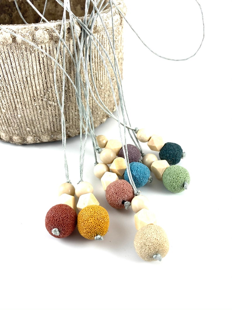 May include: A set of colorful lava stone and wooden bead necklaces. Each necklace features a variety of colors, including red, orange, yellow, green, blue, and purple. The necklaces are strung on a gray cord.