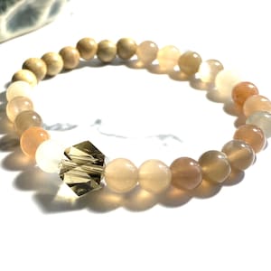 May include: A bracelet made with light brown, beige, and peach colored beads. The bracelet has a clear crystal bead in the center.