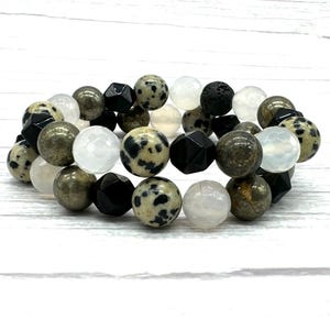 Könnte beinhalten: Ein mehrreihiges Armband mit schwarzen, weißen und braunen Perlen. Die Perlen bestehen aus verschiedenen Materialien, darunter Edelsteine, Lavastein und Holz.