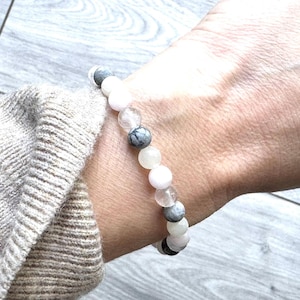 Op de afbeelding: Een armband gemaakt van witte en grijze stenen. De armband zit om een pols.