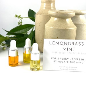 May include: Three small glass bottles with droppers filled with yellow and orange essential oil. The bottles are on a white surface with a card that reads "Lemongrass & Mint Pure Essential Oil Blend For Energy - Refresh - Stimulate the Mind www.albion-design.com Handmade in Surrey"