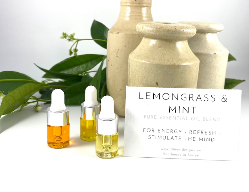 May include: Three small glass bottles with droppers filled with yellow and orange essential oil. The bottles are on a white surface with a card that reads "Lemongrass & Mint Pure Essential Oil Blend For Energy - Refresh - Stimulate the Mind www.albion-design.com Handmade in Surrey"