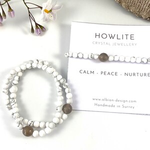May include: Two white howlite beaded bracelets with brown gemstone accents. The bracelets are stacked on top of each other. The card in the background reads "Howlite Crystal Jewellery Calm - Peace - Nurture www.albion-design.com Handmade in Surrey"