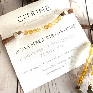 May include: Citrine oil diffuser bracelet with brown suede cord and silver beads. The card reads "Citrine Oil Diffuser Jewellery, November Birthstone, Happiness, Confidence, Positivity. Add 1-2 drops of essential oil to the wooden beads. www.albion-design.com Handmade in Surrey."
