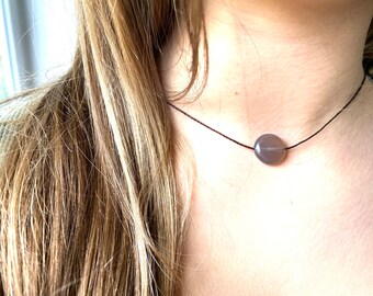 May include: A simple necklace with a single, round, gray stone pendant on a black cord.