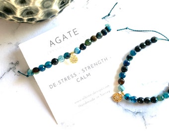 May include: Two blue agate gemstone bracelets with gold charms. The bracelets are on a white card with the text "Agate Crystal Jewelry", "De-Stress - Strength - Calm", "www.albion-design.com", and "Handmade in Surrey".