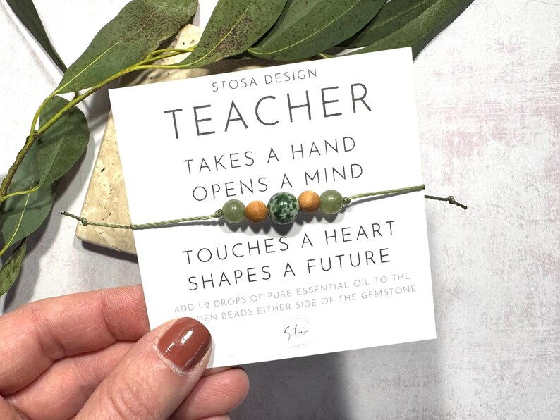 Puede incluir: Un brazalete de cuentas verdes y marrones con el texto "STOSA DESIGN TEACHER TAKES A HAND OPENS A MIND TOUCHES A HEART SHAPES A FUTURE ADD 1 2 DROPS OF PURE ESSENTIAL OIL TO THE DEN BEADS EITHER SIDE OF THE GEMSTONE Star" en una tarjeta blanca.