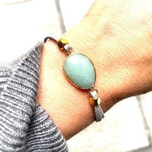 May include: A grey suede bracelet with a light green oval stone and gold accents.