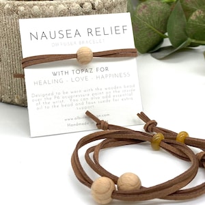 May include: Brown leather diffuser bracelet with a wooden bead and a topaz stone. The bracelet is designed to be worn over the P6 acupressure point on the inside of the wrist. The card reads "Nausea Relief Diffuser Bracelet with Topaz for Healing - Love - Happiness".