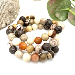 May include: A multi-coloured beaded bracelet featuring brown, white and orange stones. The bracelet is made from natural stones and has a rustic appearance.