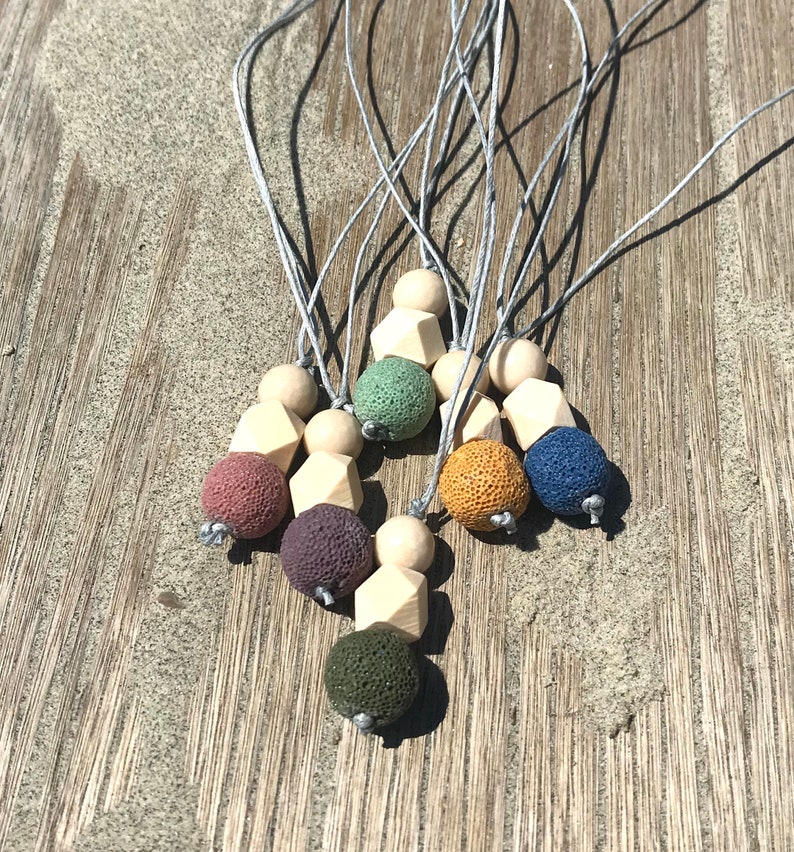 May include: A set of seven necklaces with lava stone beads and wooden beads. The necklaces are in various colors, including green, blue, brown, and yellow. The necklaces are strung on gray cords.