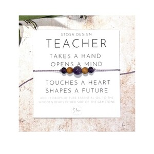 Puede incluir: Un brazalete morado y marr&oacute;n con el texto "Teacher Takes a Hand Opens a Mind Touches a Heart Shapes a Future" y "Add 1-2 drops of pure essential oil to the wooden beads either side of the gemstone".