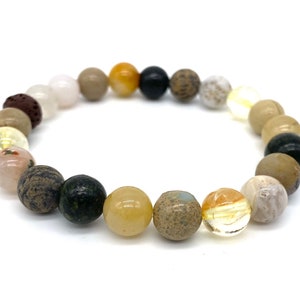 May include: A beaded bracelet with a variety of natural stones in shades of brown, beige, yellow, black, and white. The bracelet is made with round beads of different sizes and textures.