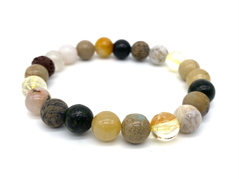 May include: A beaded bracelet with a variety of natural stones in shades of brown, beige, yellow, black, and white. The bracelet is made with round beads of different sizes and textures.