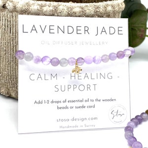 Könnte beinhalten: Lavender Jade Öldiffusor-Armband mit Lavendeljade-Perlen und einem goldenen Bienen-Anhänger. Die Karte lautet "Ruhe - Heilung - Unterstützung" und "Fügen Sie 1-2 Tropfen ätherisches Öl zu den Holzperlen oder dem Wildlederband hinzu".