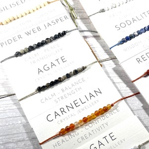Op de afbeelding: Assortiment van kleurrijke kralenarmbanden met verschillende edelsteensoorten en namen, waaronder spinnenwebjaspis, agaat, carneol, howliet, sodaliet en rode agaat. Elke armband heeft een bijbehorende beschrijving van de eigenschappen en voordelen van de steen.